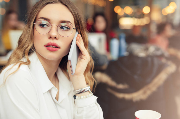 Woman Wear Glasses, Talk At Phone, Drink Her Hot Coffee While Work In Cafe On Her Laptop. Portrait Of Stylish Smiling Woman In Winter Clothes Drinking Hot Coffee And Work At Laptop. Female Winter Style. - Image - Фото, зображення
