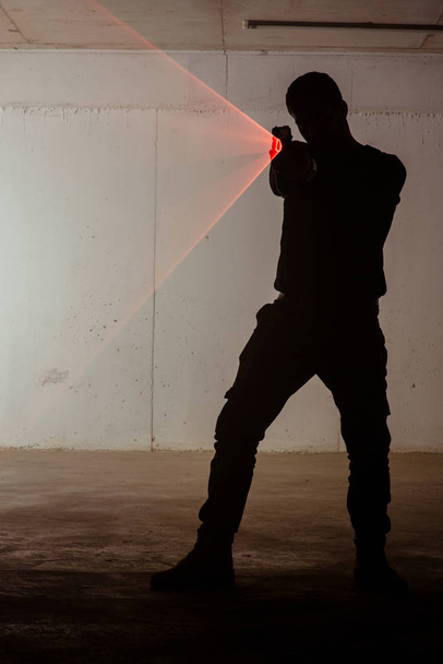 Silueta de un hombre que sostiene el revólver con láser rojo
 - Foto, imagen