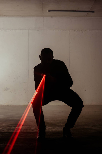 Мужчина стоит в темной комнате с лазерным пистолетом в руках
 - Фото, изображение