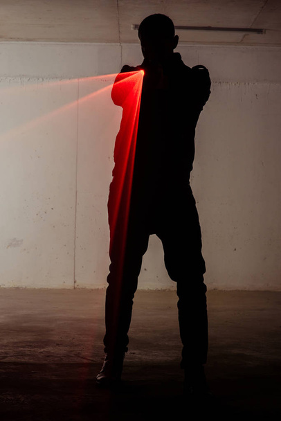 Σιλουέτα του ένα αρσενικό άτομο που στέκεται σε σκοτεινό δωμάτιο και κρατώντας όπλο με λέιζερ - Φωτογραφία, εικόνα
