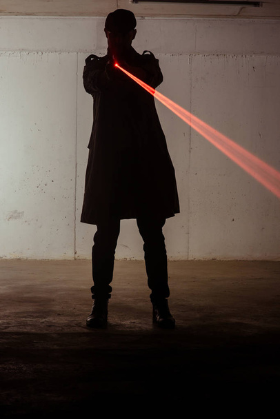 Silhueta do assassino que está de pé e segurando arma laser
 - Foto, Imagem