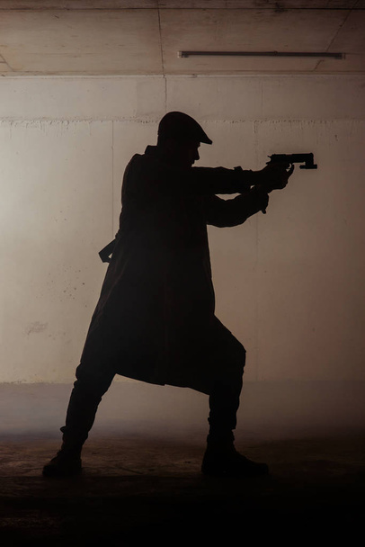 Чоловік стоїть у темній кімнаті і тримає пістолет в руках
 - Фото, зображення