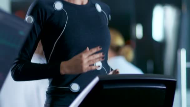 In Scientific Sports Laboratory Beautiful Woman Athlete Runs on a Treadmill with Electrodes Attached to Her Body, Monitors Show EKG Data on Display. Slow Motion. - Záběry, video