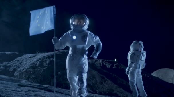 Nainen Astronautti istutus lippu Euroopan ulkomaalainen planeetta. Taustalla hänen miehistönsä jäsen, Living Station ja Exploration Rover. Avaruusmatkailun ja aurinkokunnan asuttamisen käsite
. - Materiaali, video