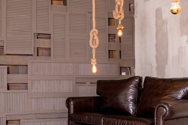 retro edison bulbs hanging, suspended to a wooden ceiling in loft, the concept of creativity.Stylish cozy scandinavian bedroom interior, leather sofa,wooden wall.loft apartment interior.Minimalist - Photo, Image