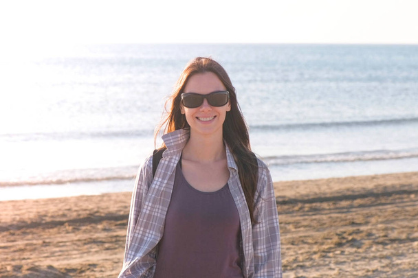 Happy young smiling brunette woman in sunglasses at sand beach by the sea. - Foto, Bild