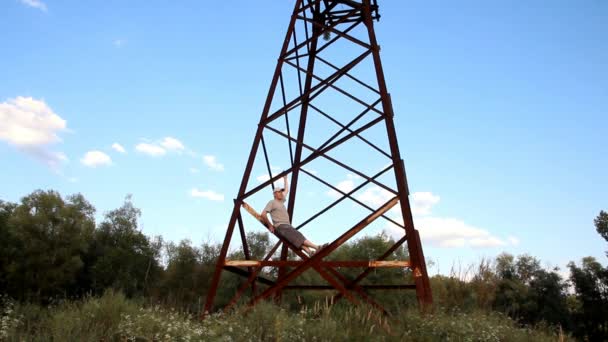 mężczyzna w szarym ubrania siedzi na słup wysokiego napięcia stary zardzewiały - Materiał filmowy, wideo