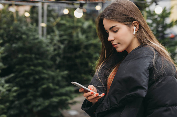 Pretty girl wear black, using phone with head phones, outdoor. Copy space - Photo, Image