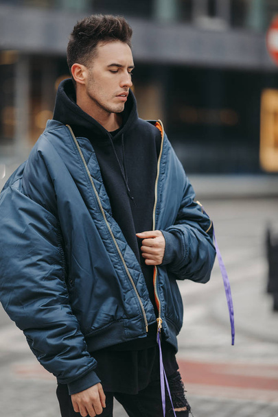 Fashionable man walk on the street near buildings. Wear blue jacket and all black. Winter, autumn outfit. Jacket with blouse and black sneakers. - Fotó, kép