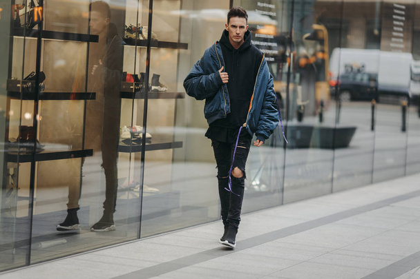 Fashionable man walk on the street near buildings. Wear blue jacket and all black. Winter, autumn outfit. Jacket with blouse and black sneakers. - Foto, Imagem