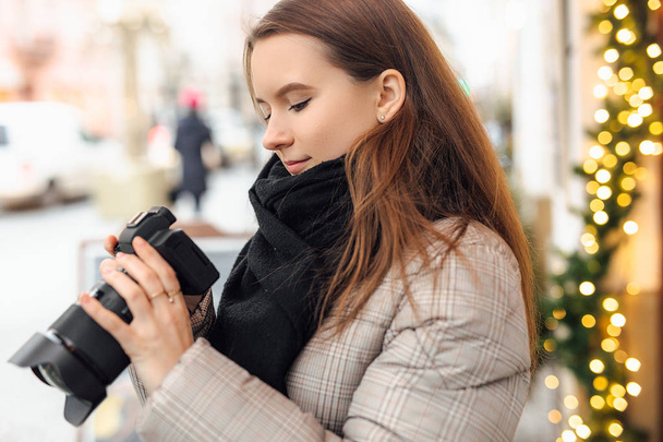 Photographer girl walk in the street and take photos in camera with happy face. Wear black scarf. Winter, autumn outfit. - Foto, Bild