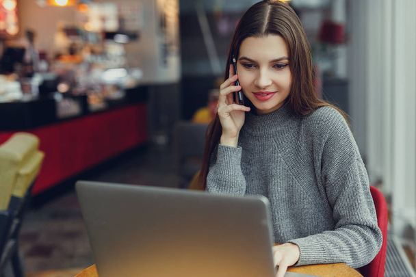 Trzy poziomy. Młoda kobieta siedzi w tabeli i porozmawiać o jej telefon patrząc na laptopa. Kobieta pracuje w kawiarni. Blogger. -Obraz - Zdjęcie, obraz