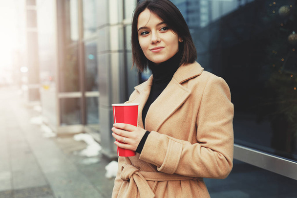 Kobiety piją jej gorącej kawy podczas spaceru na ulicy. Portret stylowy uśmiechający się kobiety w zimowe ubrania picia gorącej kawy. Kobiet zima styl. -Obraz - Zdjęcie, obraz