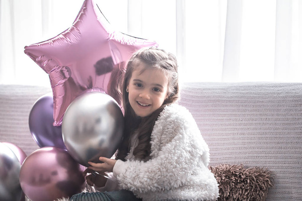 little girl with balloons sitting on the couch, holiday concept - Фото, изображение