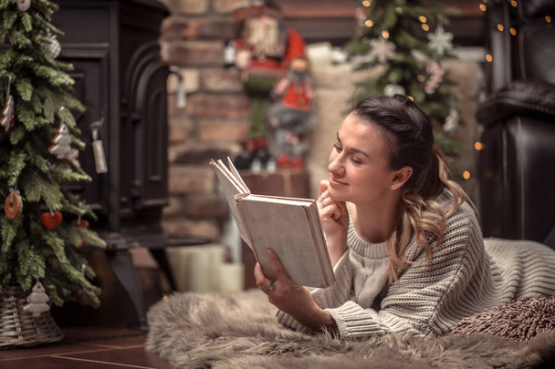 διαβάζοντας ένα βιβλίο σε μια ζεστή ατμόσφαιρα στο σπίτι κοντά στο τζάκι, η έννοια της σπίτι υπόλοιπο κορίτσι - Φωτογραφία, εικόνα