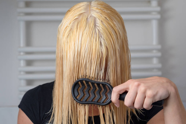 Блондинка расчесывает свои длинные мокрые волосы после мытья их в ванной комнате с фронтальным видом, прикрывая лицо.
 - Фото, изображение