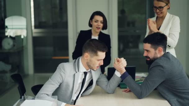 Bebaarde jongeren kantoor werknemers ondervindt plezier beoefenen van arm worstelen terwijl vrouwen kijken en hen steunen dan doen high-five en handen klappen. - Video