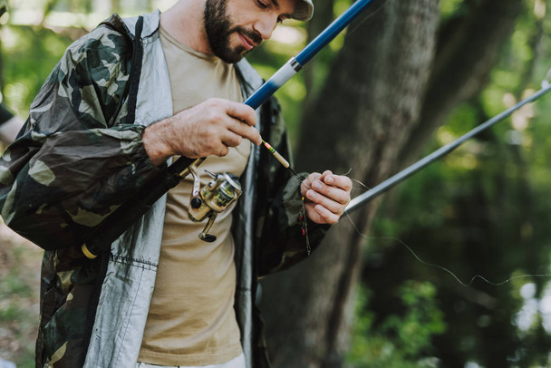 Pleasant bearded man fixing the hook of his rod - Foto, imagen