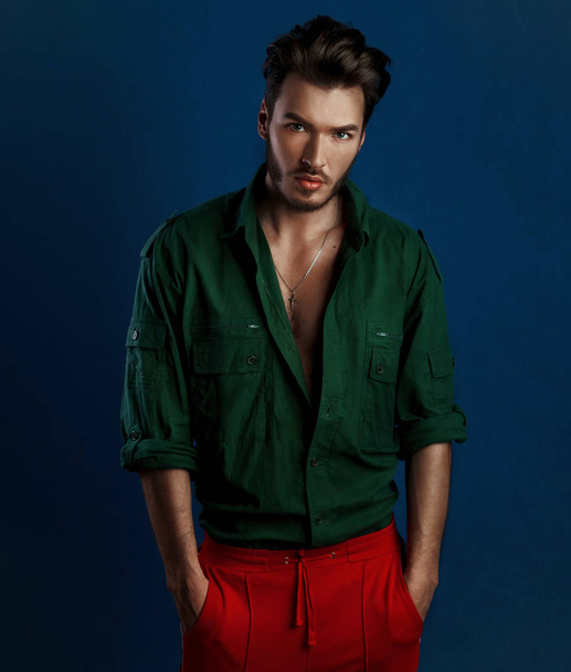 Módní portrét mladého muže v zeleném tričku a červené kalhoty pózy tmavě modrá zeď s kontrastním světlem - Fotografie, Obrázek