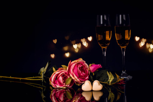 Два бокала шампанского, розы и два шоколада в форме сердца на черном фоне. Любовь, День святого Валентина
 - Фото, изображение