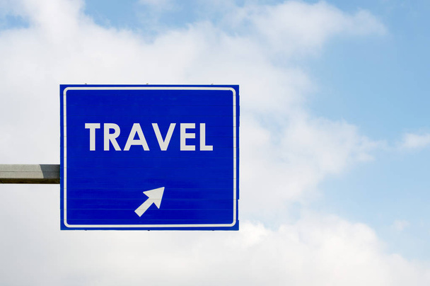 青い空と白い雲の背景に旅行単語を表示する青い道路標識 - 写真・画像