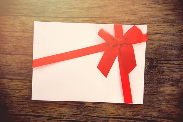 Δώρο κάρτα σε φόντο ξύλινη / ροζ λευκό δωροκάρτα διακοσμημένα με κόκκινη κορδέλα φιόγκο διακοπών χαρούμενα Χριστούγεννα ευτυχισμένο το νέο έτος ή ημέρα του Αγίου Βαλεντίνου δώρο κουπόνι στο ύφος στυλ vintage παρασκήνιο κάτοψη - Φωτογραφία, εικόνα