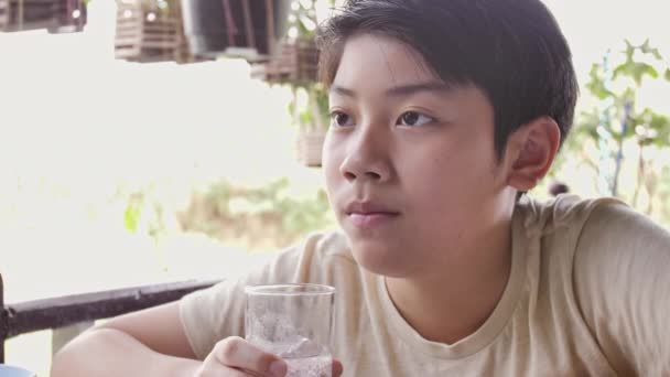 Slow motion van Aziatische jongen drinkt water uit een glas na het ontbijt, close-up tiener jongen met glas water. - Video