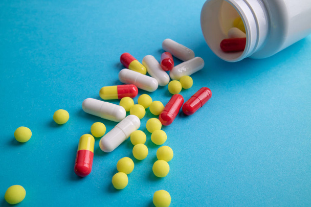 Comprimidos misturados derramados da garrafa branca. Medicina Farmacêutica comprimidos, cápsulas e comprimidos no fundo azul
 - Foto, Imagem