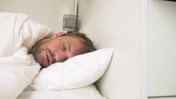 zieke jongeman met koorts in slaap in bed, gedekt door een deken - Foto, afbeelding