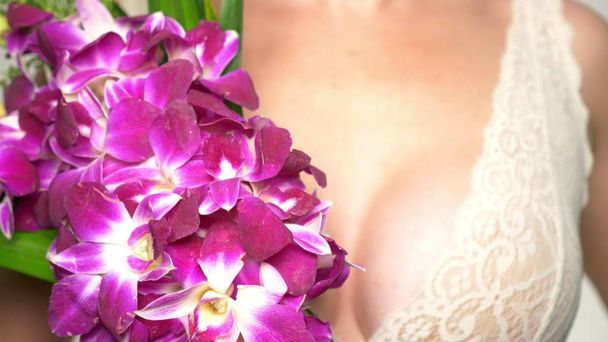 close-up. female breast closeup with a large bouquet of orchids in their hands. female breast health concept - Zdjęcie, obraz