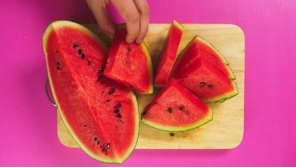 top view, female hand cuts fruit with a knife on a wooden board, red watermelon. The concept of natural healthy food. - 写真・画像
