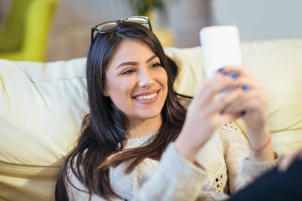 πορτρέτο της νεαρής γυναίκας χαμογελαστά χρησιμοποιώντας το smartphone στο σπίτι - Φωτογραφία, εικόνα