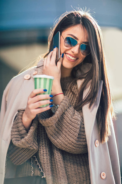 portret uśmiechający się młoda kobieta z kawą do przejdź rozmawiać na smartphone na ulicy - Zdjęcie, obraz