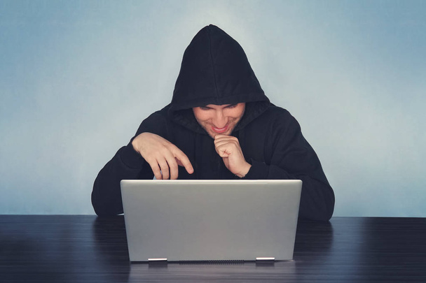 Ein fröhlicher Hacker mit schwarzer Kapuze schnappt sich das Passwort. Wer eine Webseite hackt, stiehlt Geld. das Konzept der Cyber-Kriminalität und das Hacken elektronischer Geräte - Foto, Bild