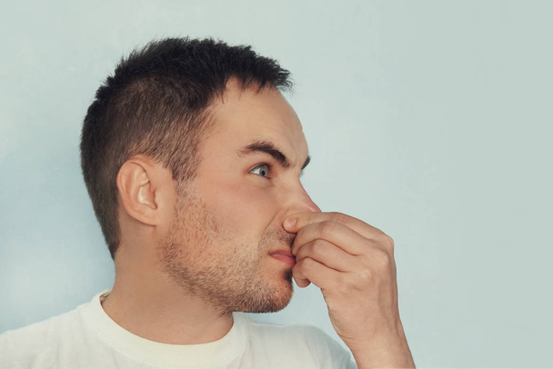 portrait of a man closes his nose, smells bad, on a blue background.. guy's plugging his nose to sneeze. cold. - Photo, Image