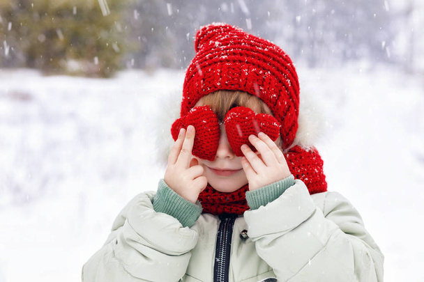 Dítě ve světlé oblečení je stojící uprostřed sněhové vločky a drží dvě malé červené srdce před jejíma očima s její prsty na zimní pozadí. Koncept je Svátého den. - Fotografie, Obrázek