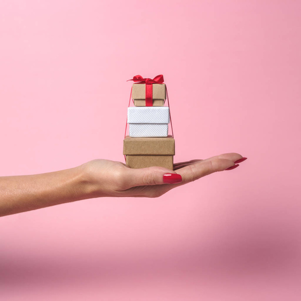 Womans hand holding gift boxes on pink background. Minimal sale concept. - Фото, изображение