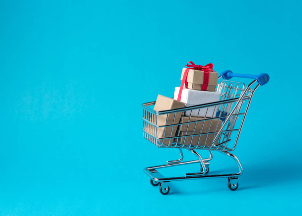 Gift boxes in shopping cart on blue background. Minimal sale concept. - Фото, зображення