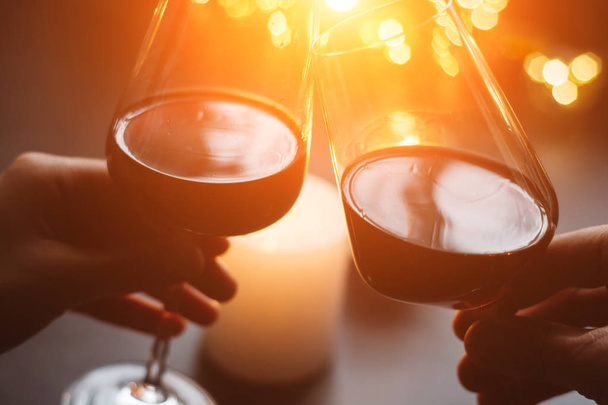 Two glasses of wine red in hand on the background candle and garlands. Valentines day - Foto, imagen