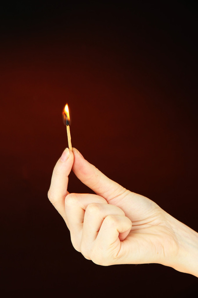 Burning match in female hand, on dark brown background - Fotografie, Obrázek