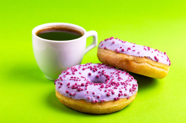 Two delicious lilac donuts with sprinkle and cup of coffee on bright green background. Unhealthy, but tasty sweets. Copy space. Horizontal view - Foto, immagini
