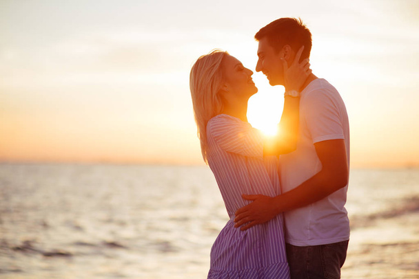 Young happy couple on seashore in the lights of sunset. - Fotoğraf, Görsel