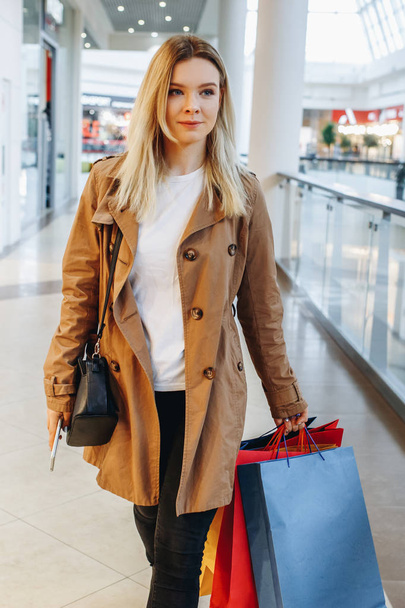 金髪少女はショッピング バッグとモールを歩いて彼女の携帯電話で何かをタイプします。概念: ショッピング、販売、消費者のライフ スタイルのイメージ - 写真・画像