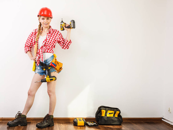 Woman wearing helmet using drill. Girl working at flat remodeling. Building, repair and renovation. - Φωτογραφία, εικόνα