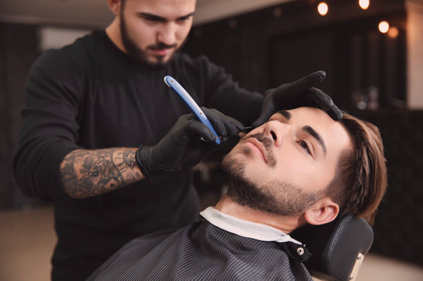 Professional hairdresser shaving client with straight razor in barbershop - Photo, image