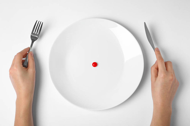 Woman holding cutlery near plate with weight loss pill on white background, top view - Fotoğraf, Görsel