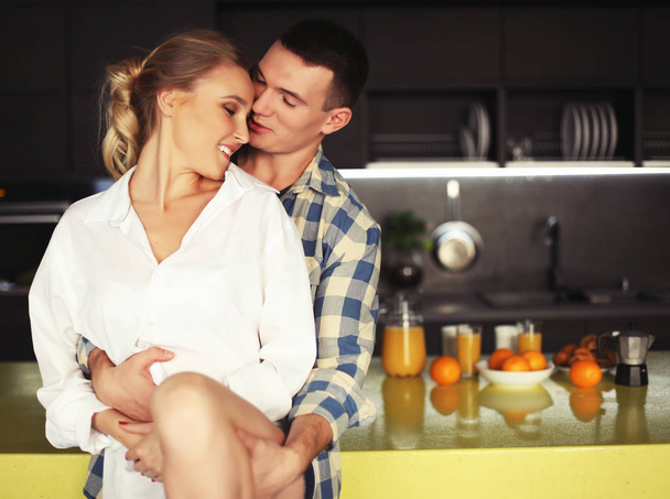 Lovely young couple standing and hugging on a kitchen at home - 写真・画像