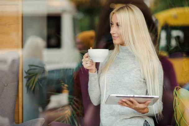 Η γυναίκα στο café κάθεται κοντά στο παράθυρο και πίνει καφέ με ευχαρίστηση - Φωτογραφία, εικόνα