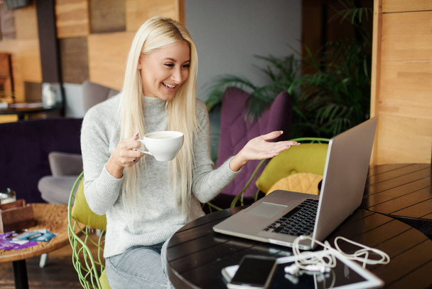 Concentrado en el trabajo. Mujer joven con confianza en ropa casual inteligente trabajando en el ordenador portátil mientras está sentado cerca de la ventana en la oficina creativa o cafetería. Tomando una taza de café
 - Foto, imagen