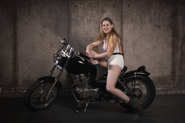 Ποδηλάτης όμορφο κορίτσι σε μια μοτοσικλέτα σε ένα άδειο-Γκαράζ-Βουλκανιζατέρ - Φωτογραφία, εικόνα